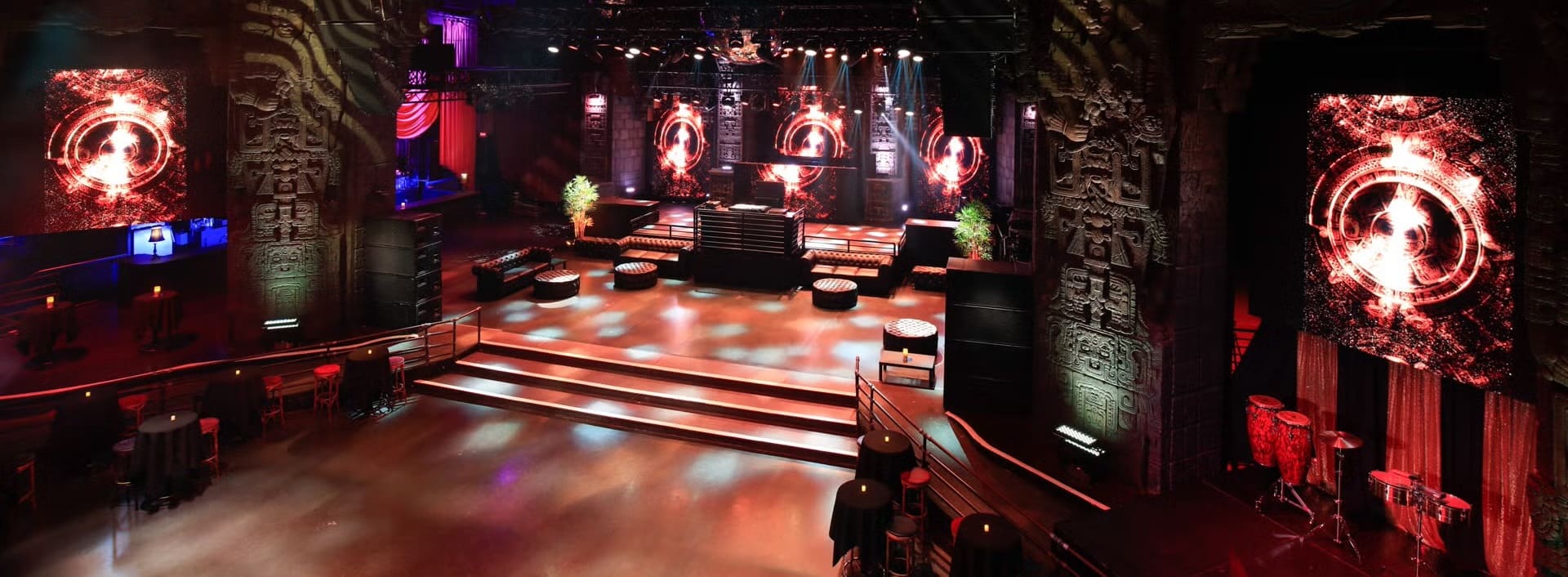 Empty nightclub venue with large stage, LED screens, dramatic lighting, and Aztec-style architectural details